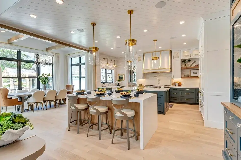 Bright and airy luxury kitchen with dining space, white and navy cabinetry, and sophisticated lighting in a custom home by E Builders, highlighted in the 2020 Utah Valley Parade of Homes