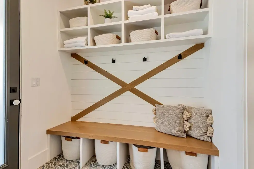 Farmhouse-style mudroom with a built-in wooden bench, X-shaped wood accents, and woven storage baskets in a custom home by E Builders, featured in the 2020 Utah Valley Parade of Homes