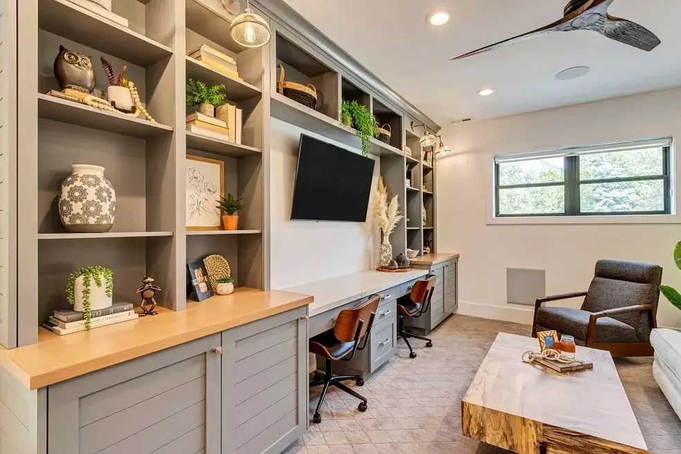 Functional home library and workspace with built-in gray shelves, a TV, and a modern desk in a custom home by E Builders, featured in the 2020 Utah Valley Parade of Homes