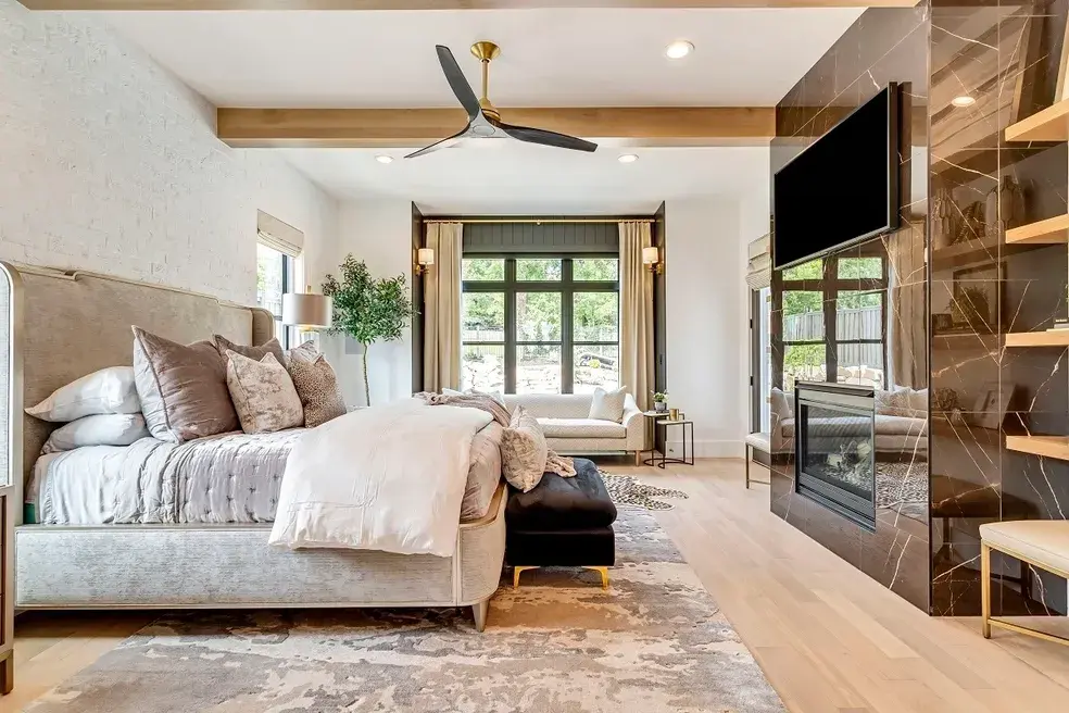 Luxurious master bedroom with a modern fireplace, large windows, and a cozy seating area in a custom home by E Builders, featured in the 2020 Utah Valley Parade of Homes