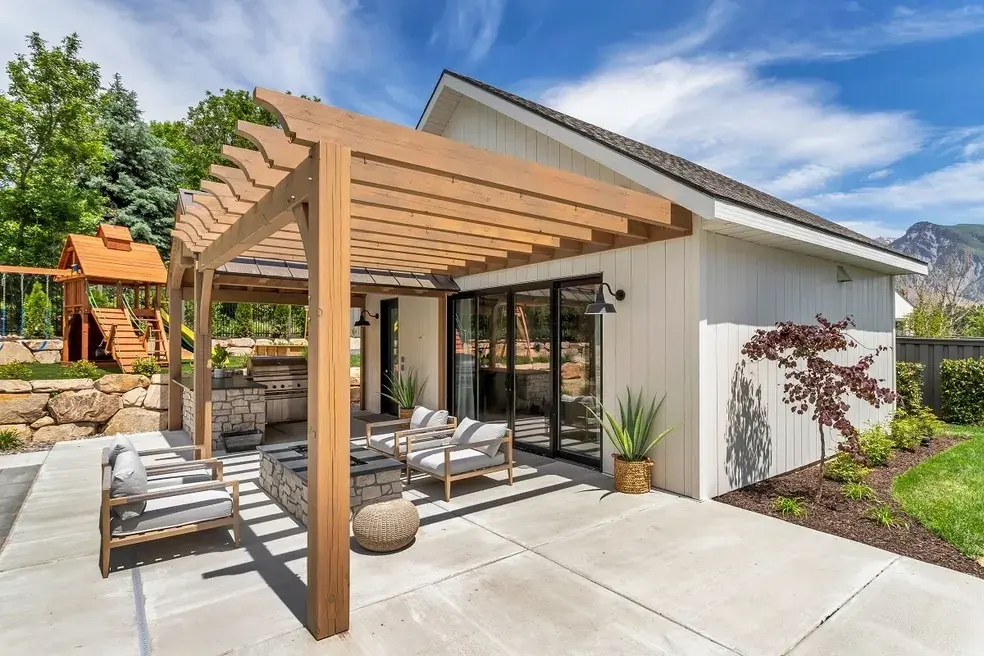 Modern outdoor living area with a pergola-covered patio, lush landscaping, and comfortable seating in a custom home by E Builders, highlighted in the 2020 Utah Valley Parade of Homes