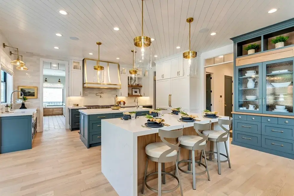 Open-concept kitchen with a large white island, blue cabinetry, and gold pendant lights in a custom home by E Builders, featured in the 2020 Utah Valley Parade of Homes