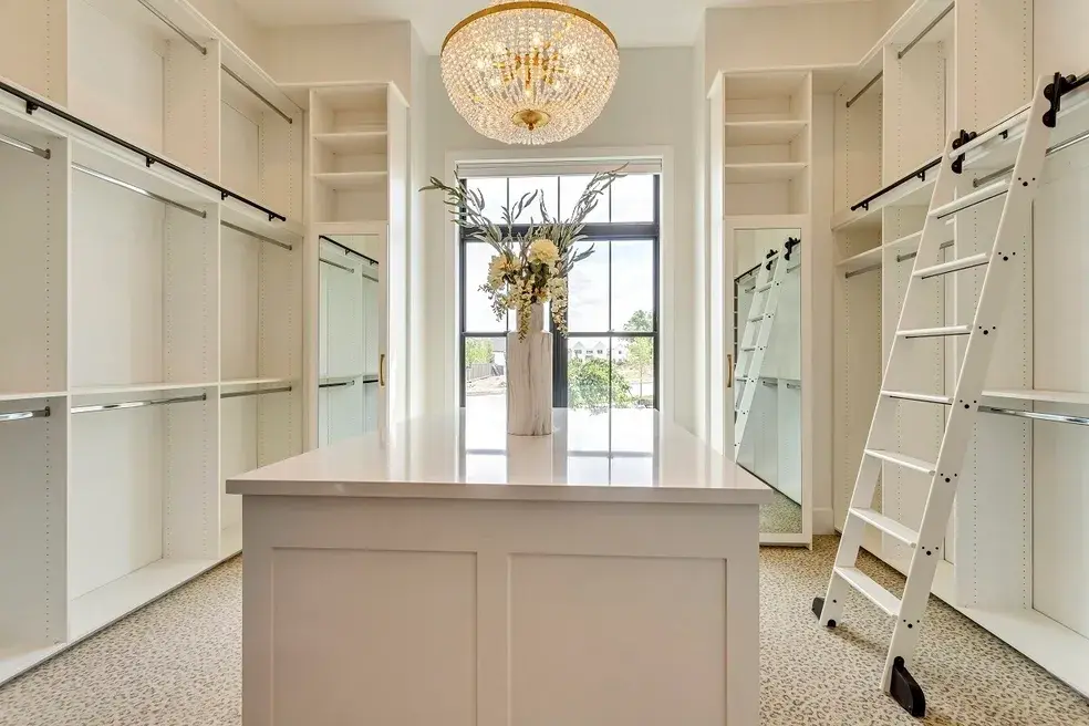 Spacious master closet with an island, gold-accented chandelier, and natural light in a custom home by E Builders, showcased in the 2020 Utah Valley Parade of Homes
