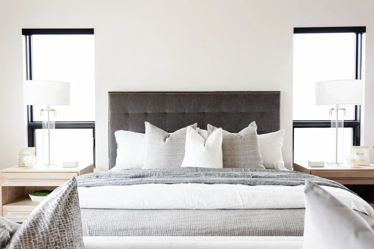 Serene bedroom with a gray tufted headboard and neutral bedding in a contemporary custom home in Utah by E Builders