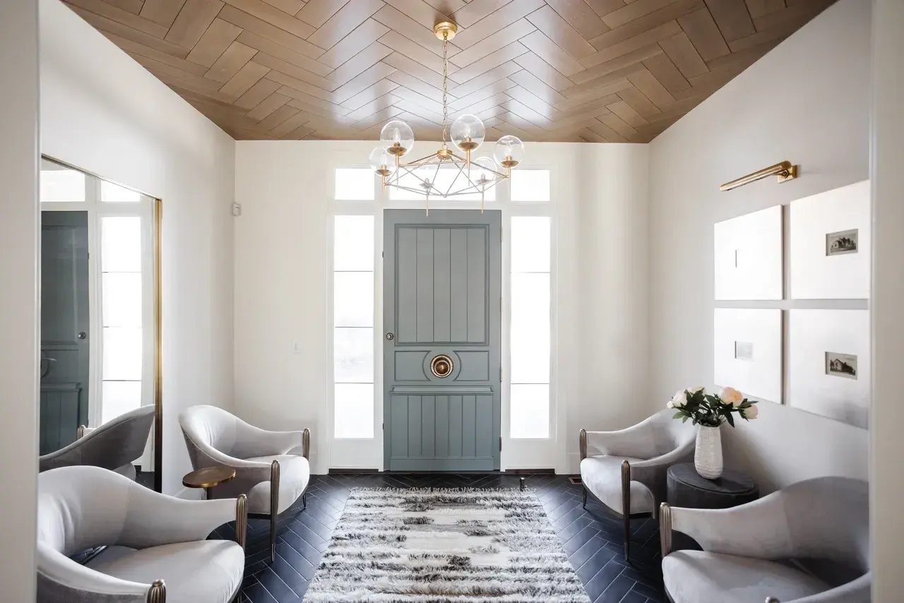 Elegant foyer design with a custom blue entry door, white seating, and statement chandelier in a Draper, Utah luxury home by E Builders