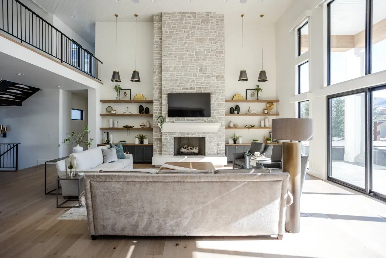 High-ceiling living room featuring a floor-to-ceiling stone fireplace, large windows, and a cozy seating area in a Draper, Utah luxury home by E Builders