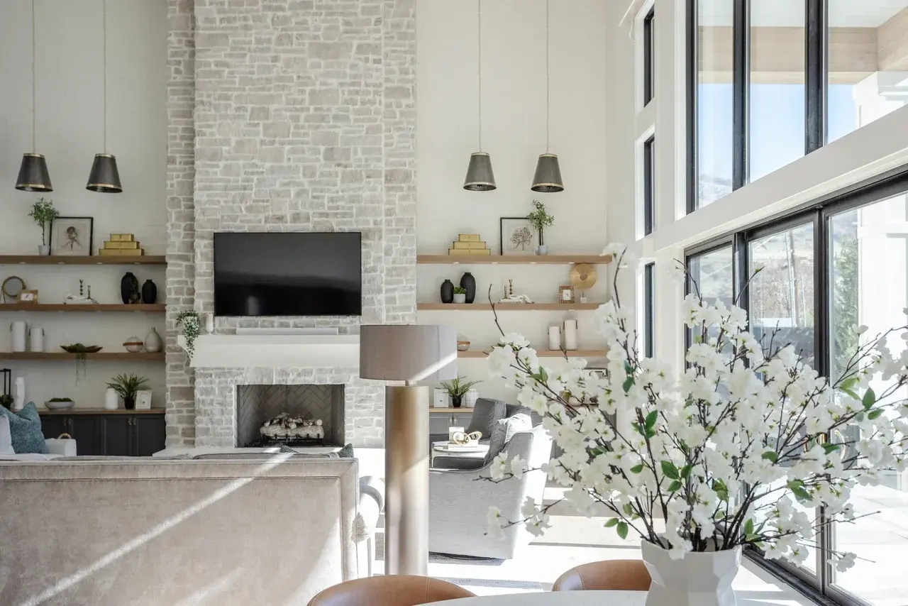 High-ceiling living space featuring a stone fireplace, open shelving, and natural light in a Draper, Utah luxury home by E Builders