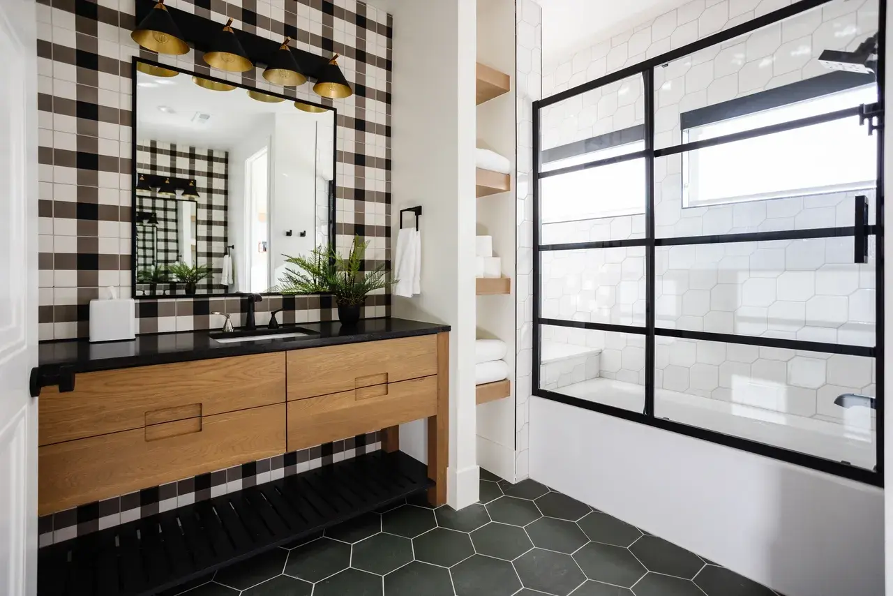 Modern bathroom featuring a black-framed glass shower, plaid accent wall, and geometric tile flooring in a luxury custom home in Draper, Utah by E Builders