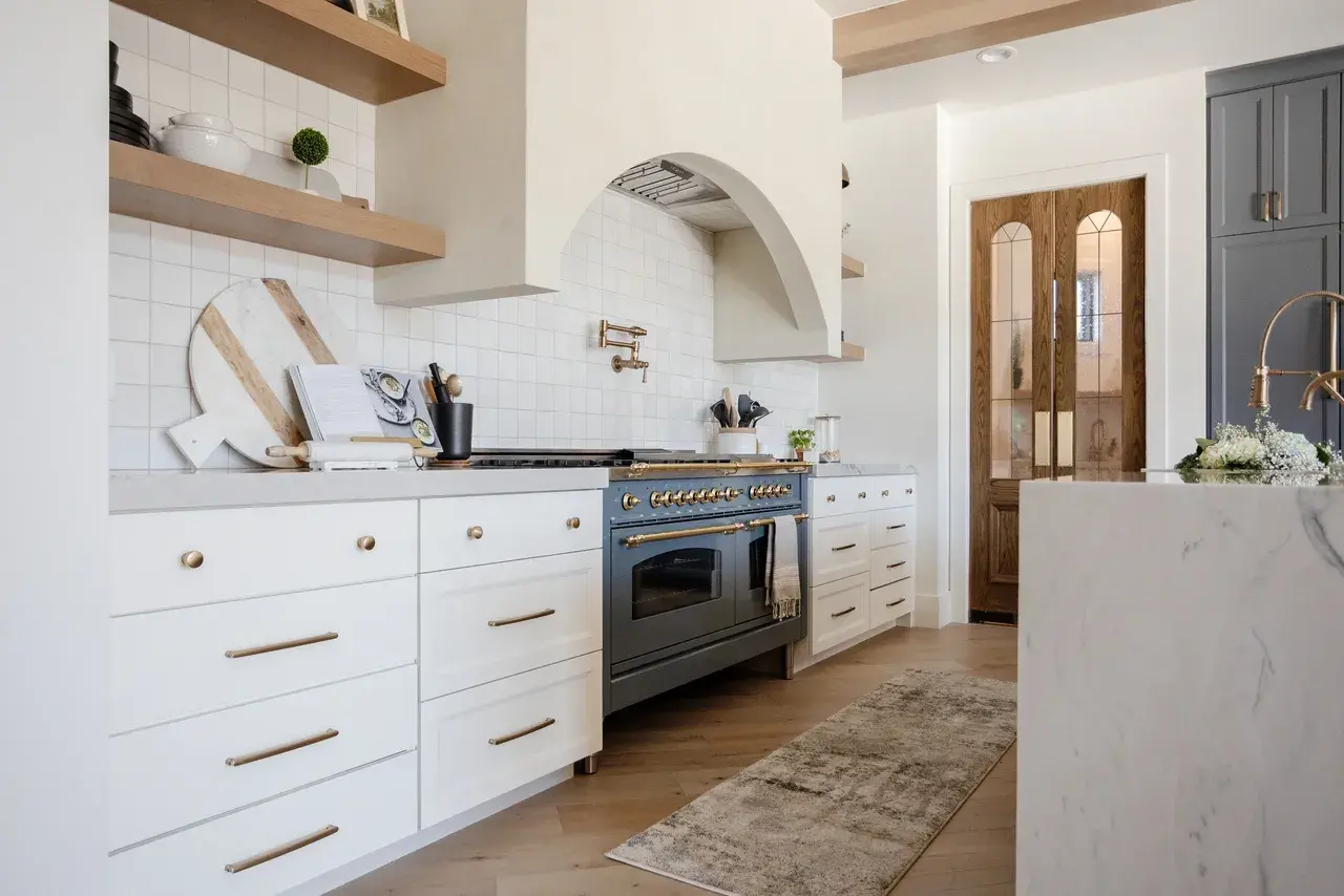 Modern kitchen with a European-style range, arched hood, and brass accents in a luxury custom home in Draper, Utah by E Builders