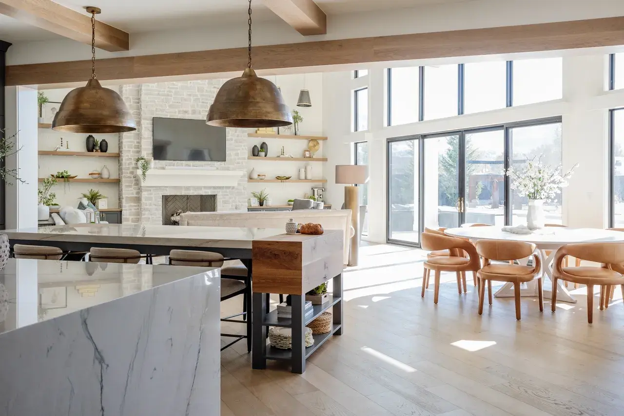 Open-concept kitchen and living space with floor-to-ceiling windows and a stone fireplace in a luxury custom home in Draper, Utah by E Builders