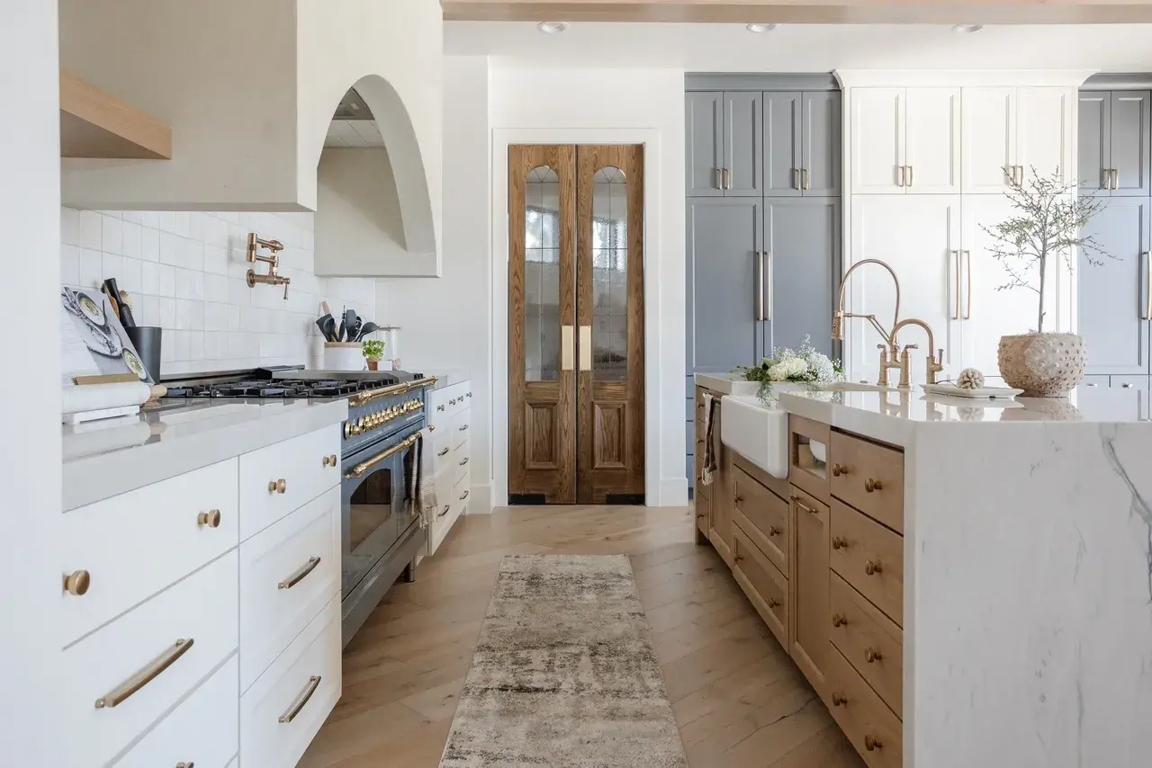 Stunning kitchen design with white and blue cabinetry, arched range hood, and custom wood pantry doors in a luxury custom home in Draper, Utah by E Builders