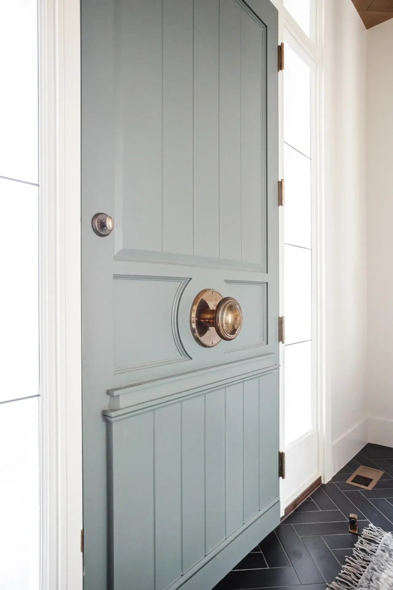 Stylish Dutch-style entry door with panel detailing and warm brass accents in a luxury custom home in Draper, Utah by E Builders