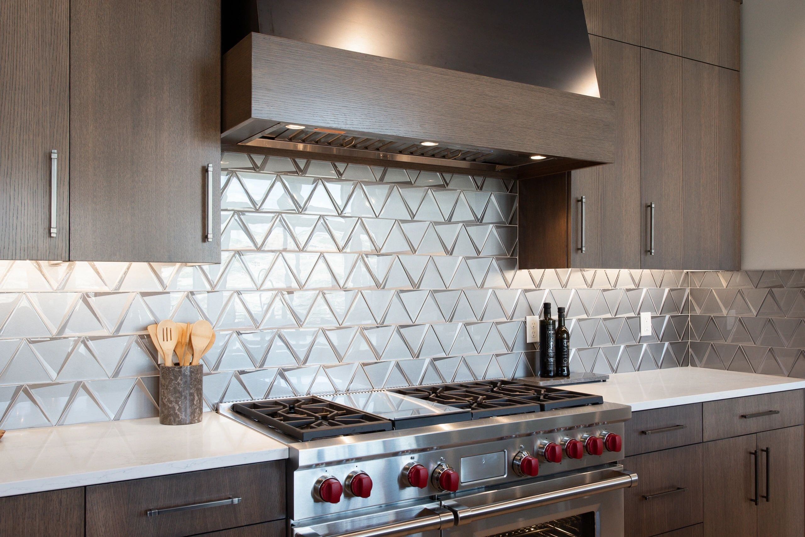 Geometric tile backsplash and gas range with red knobs in a custom home in Park City, Utah by E Builders