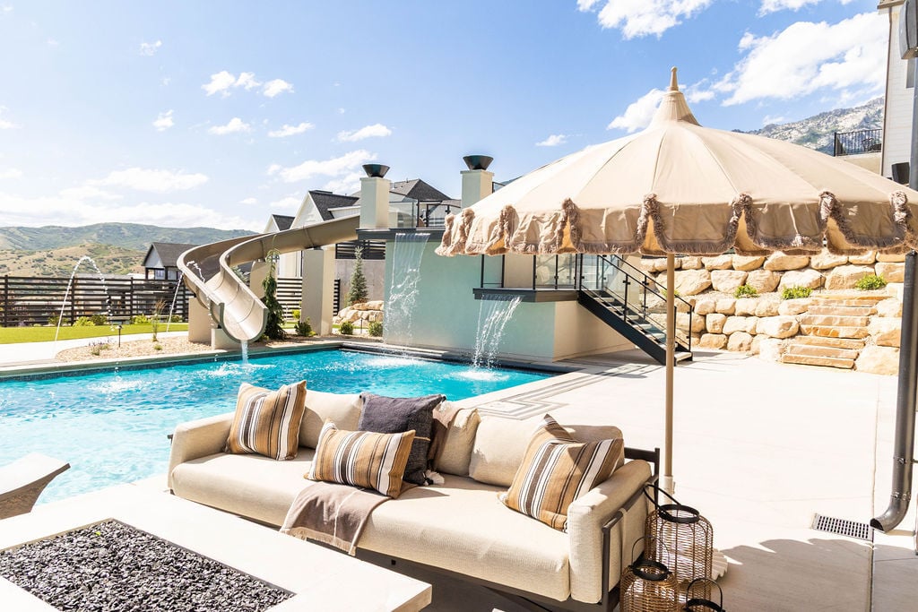 Backyard oasis featuring a waterslide, sun loungers, and mountain views in the Room with a View custom home featured in the 2025 Utah Valley Parade of Homes by E Builders
