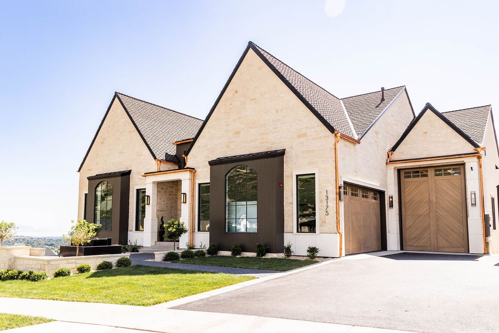 Complete exterior view showcasing warm tones, copper accents, and custom garage doors of the Room with a View custom home featured in the 2025 Utah Valley Parade of Homes by E Builders