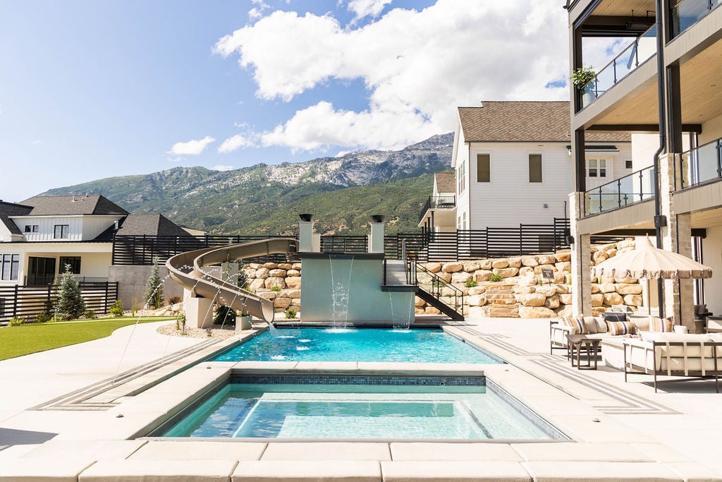 Luxury outdoor pool design with waterslide and integrated spa of the Room with a View custom home featured in the 2025 Utah Valley Parade of Homes by E Builders