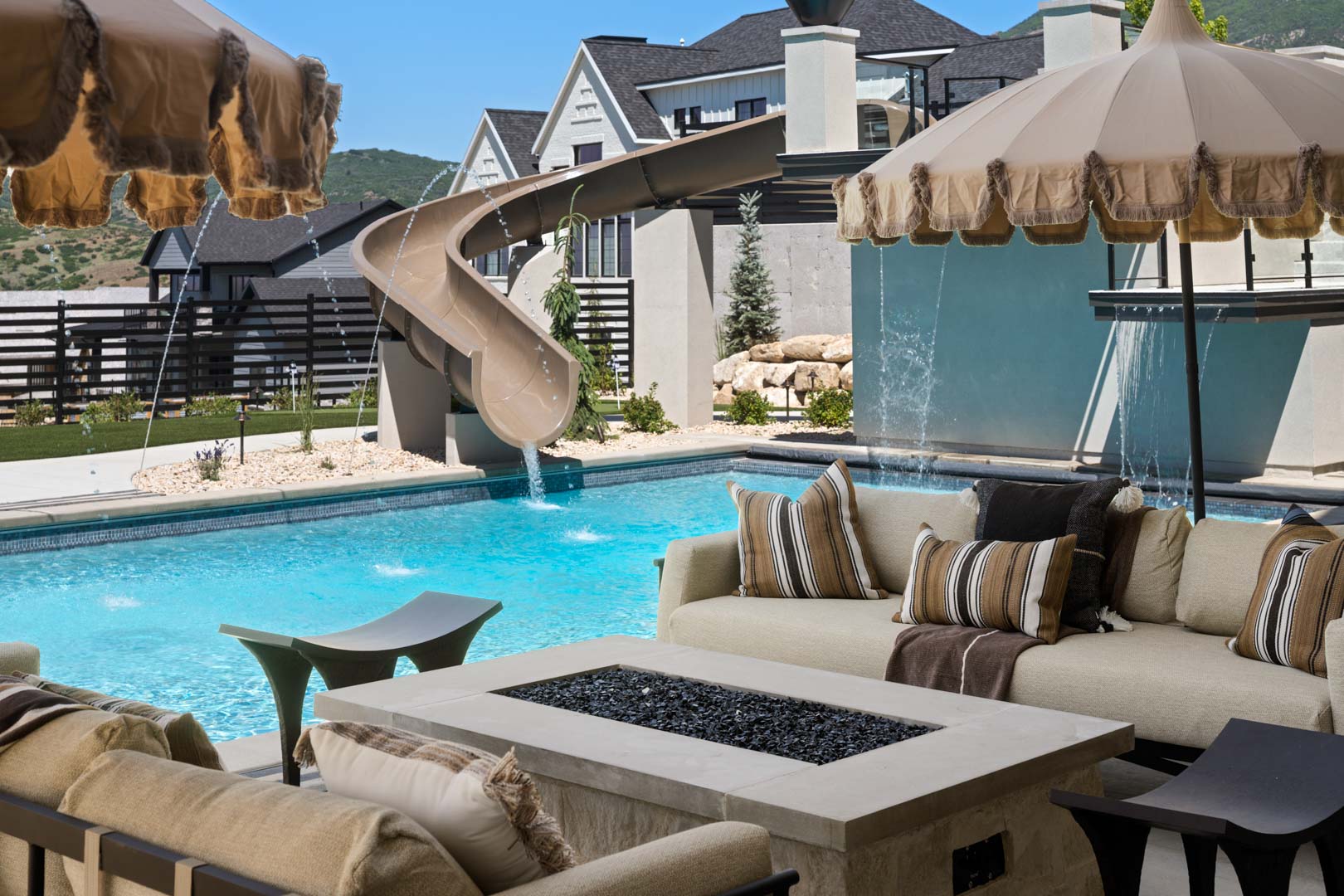 Poolside lounge area with umbrellas and firepit in custom home Room with a View featured in the 2025 Utah Valley Parade of Homes by E Builders