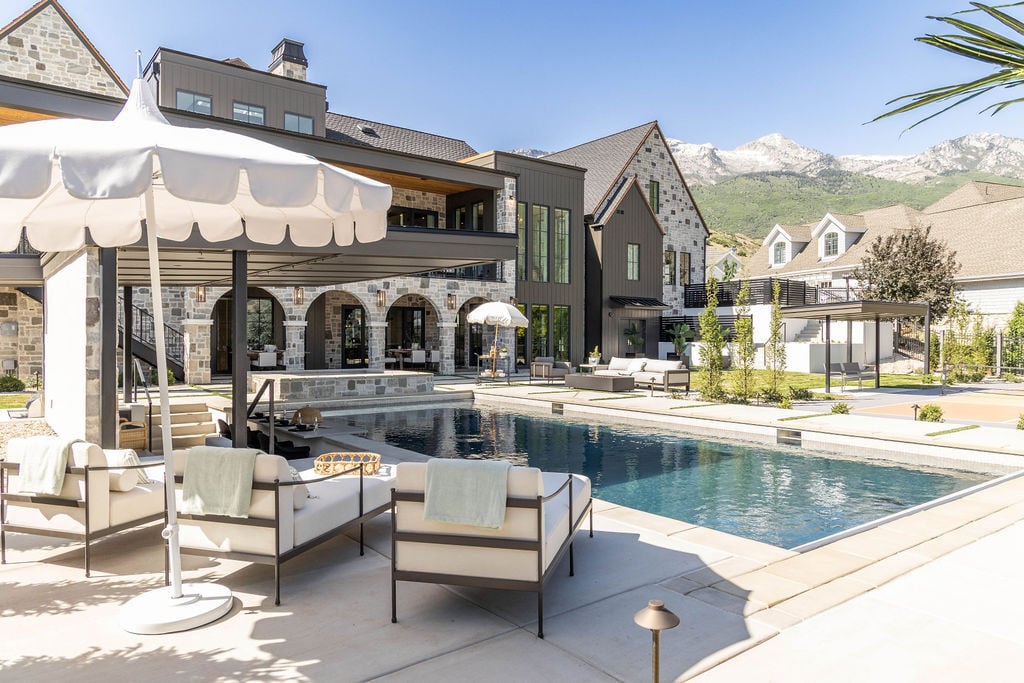 Backyard lounge and pool deck with umbrellas and mountain views in a custom home featured in the 2025 Utah Valley Parade of Homes