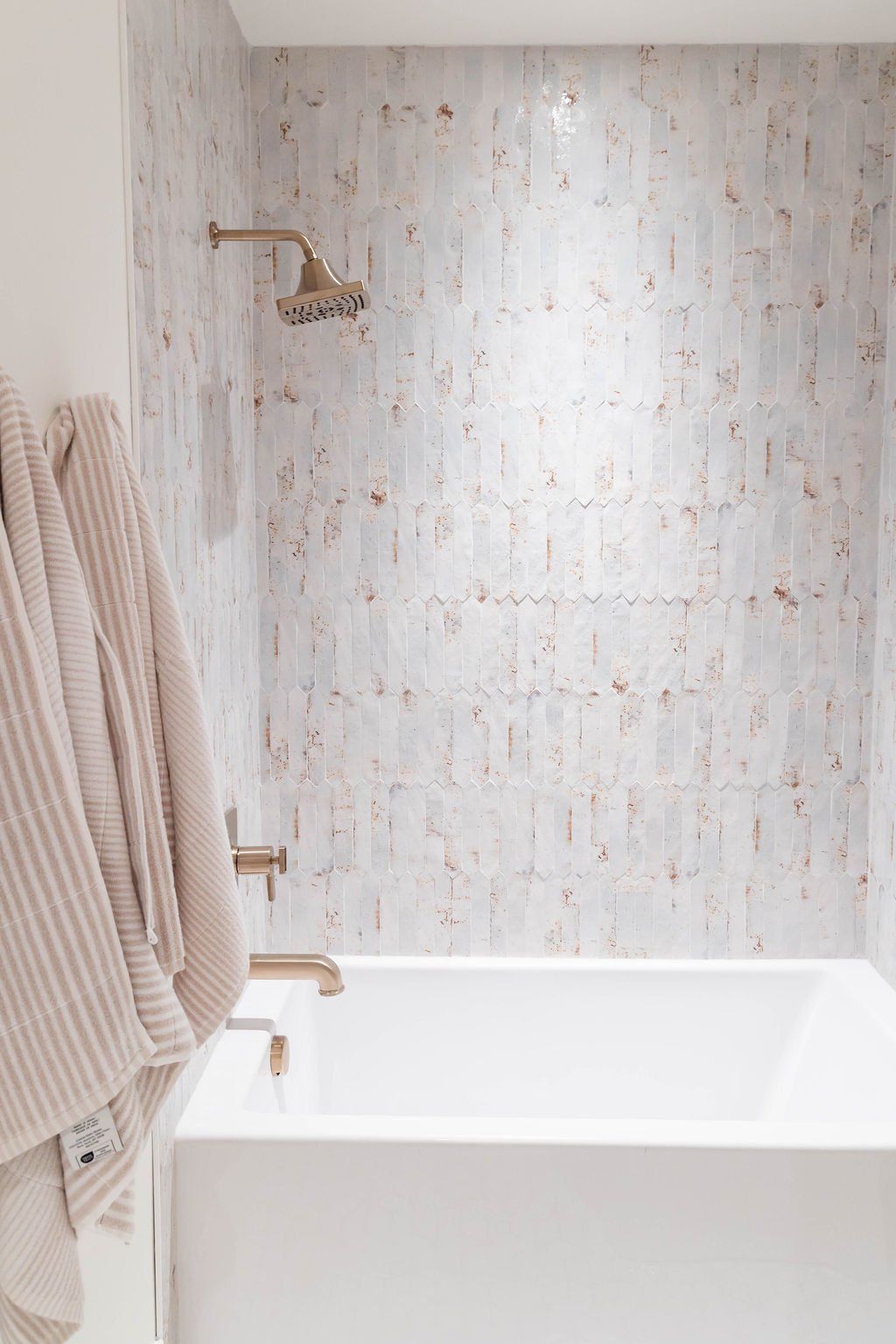 Contemporary bathtub area with textured tile and gold fixtures in a custom home featured in the 2025 Utah Valley Parade of Homes