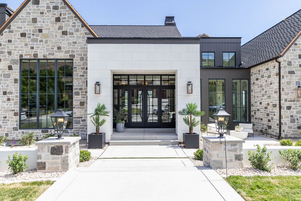 Front entrance of luxury custom home with mixed stone cladding and black-framed windows, featured in the 2025 Utah Valley Parade of Homes