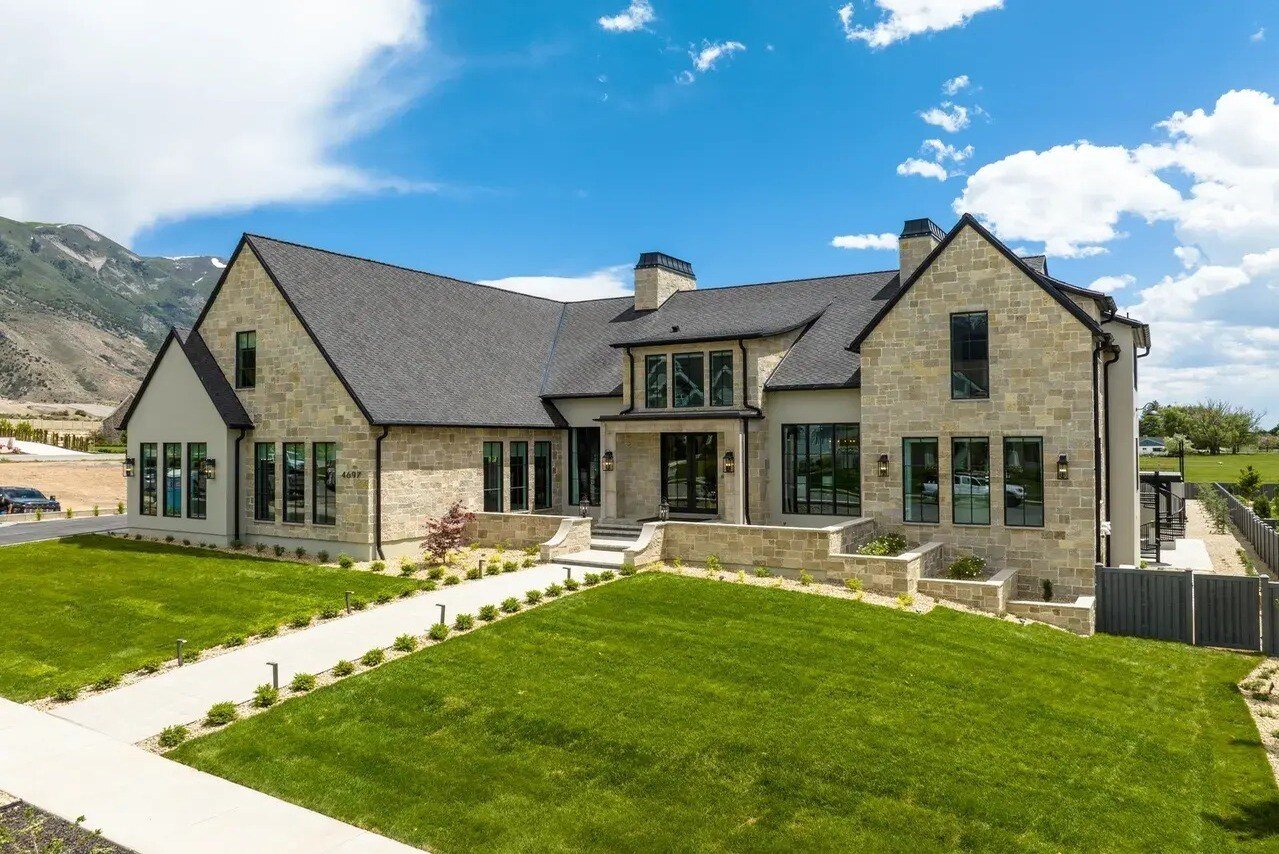 The elegant front facade of Hillside Haven custom home by E Builders, with a grand entryway, lush landscaping, and stone exterior, part of the 2023 Utah Valley Parade of Homes